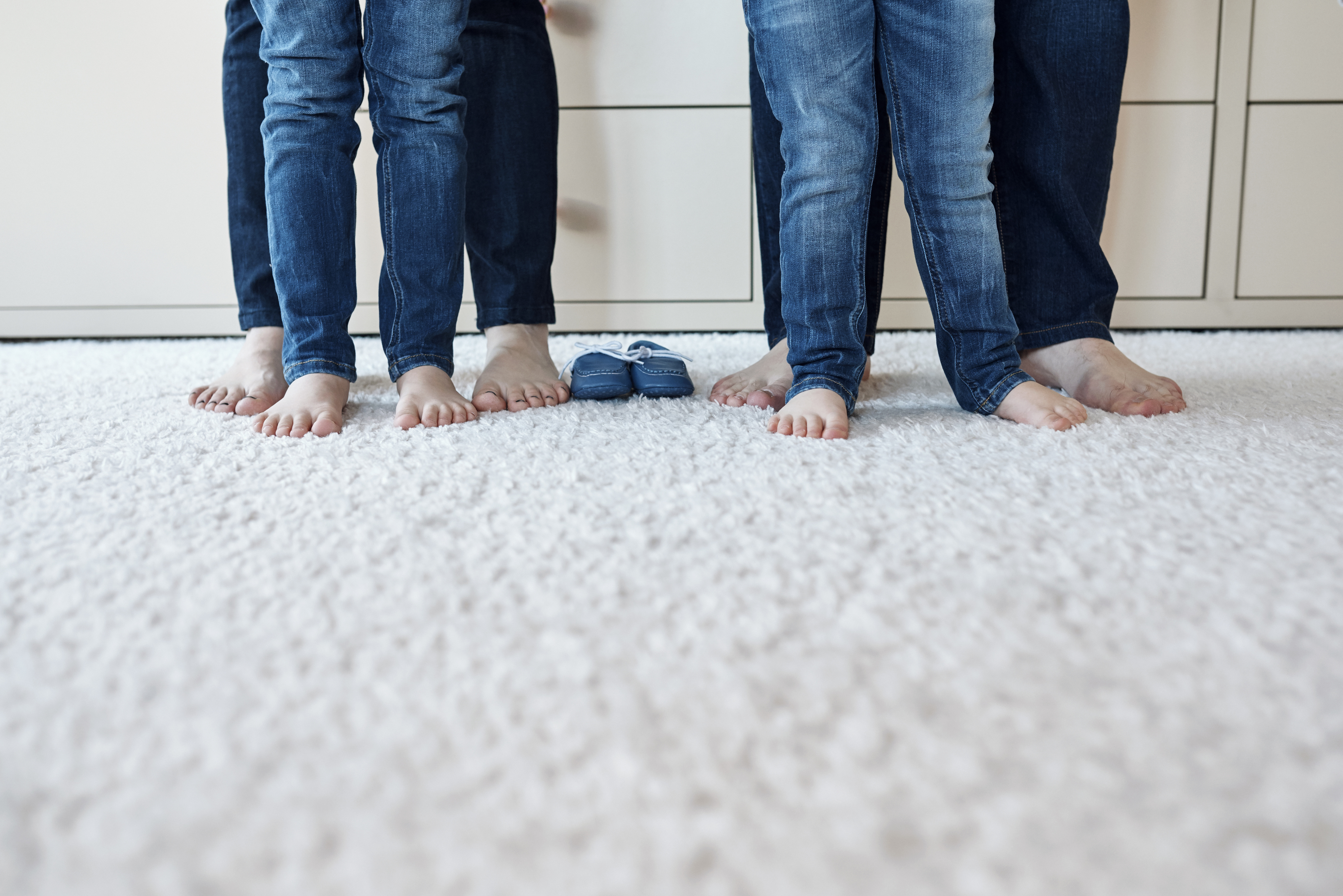 daughters, mother and father barefoot legs wearing jeans.photo taken in bedroom, unrecognizable persons.